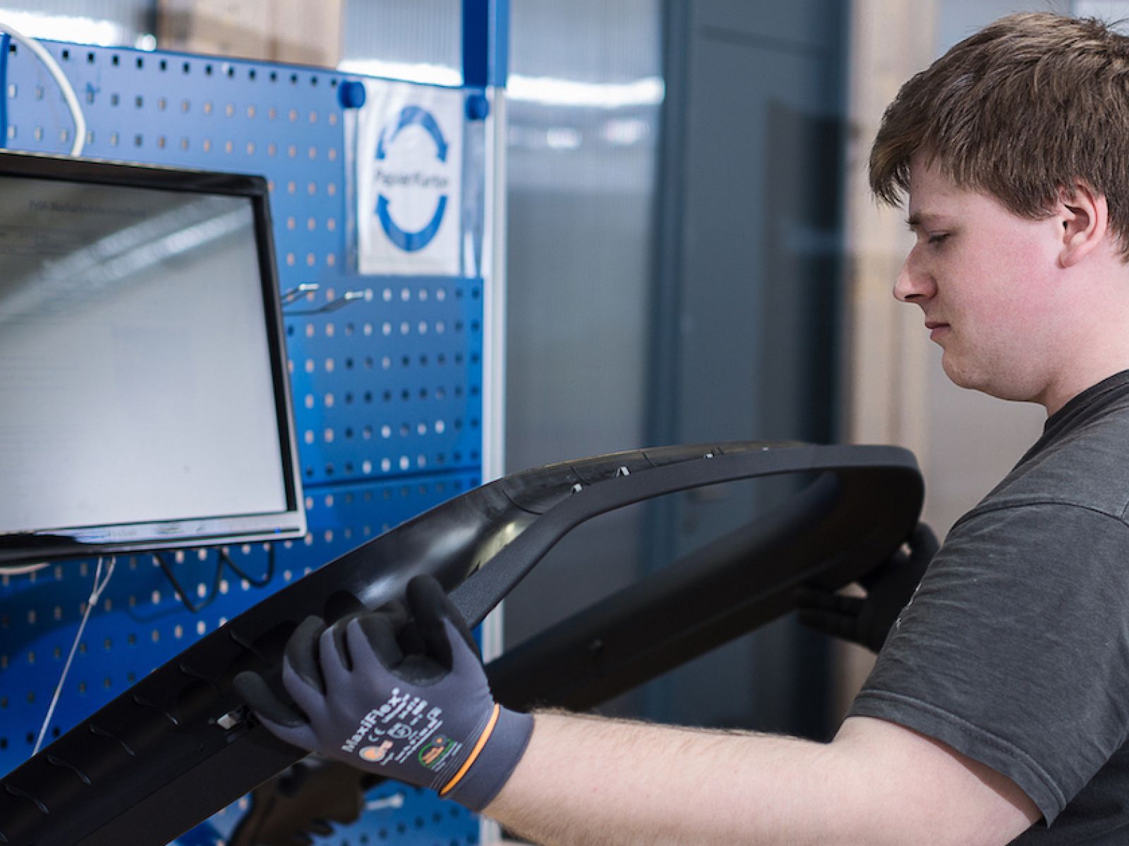 Ein Mitarbeiter von EuroQ prüft ein Autoteil an einem Arbeitsplatz mit Monitor für Kontrolle und Nacharbeiten.